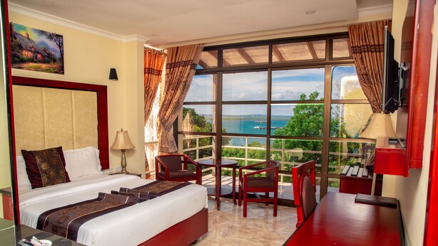 Ein Hotelzimmer mit einem großen Bett, einem Schreibtisch, einem Sessel und Meerblick.
