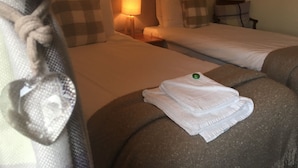 A hotel room with two beds, a nightstand, a lamp, and a towel on the bed. - The Herdwick Inn (Penrith)