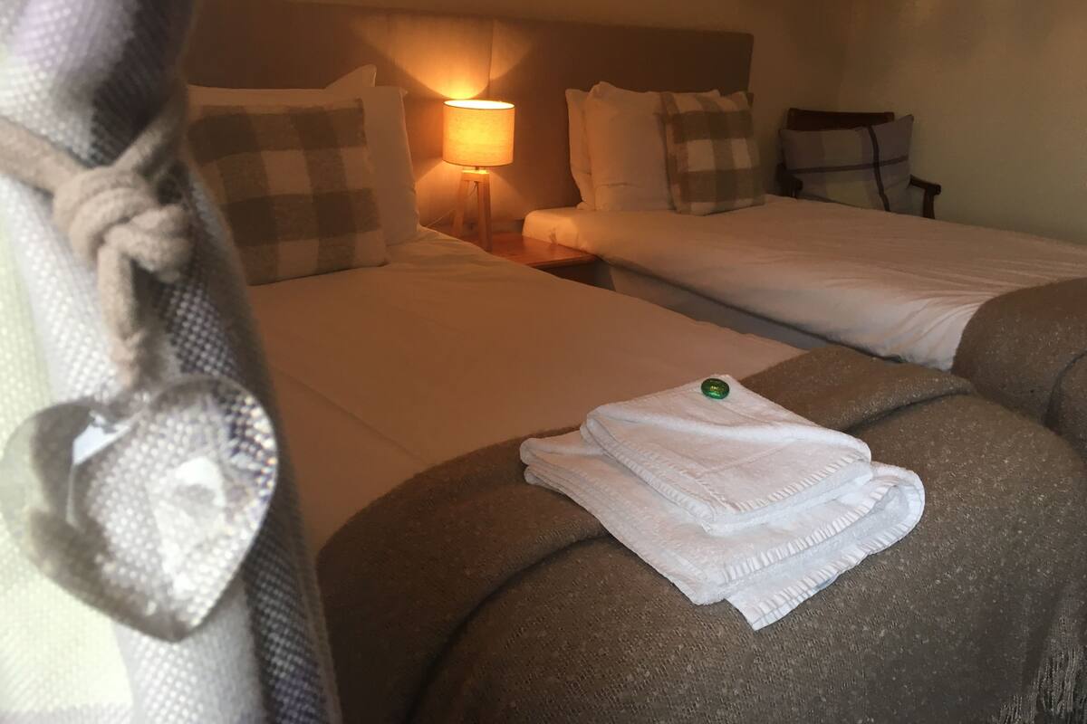 A hotel room with two beds, a nightstand, a lamp, and a towel on the bed.
