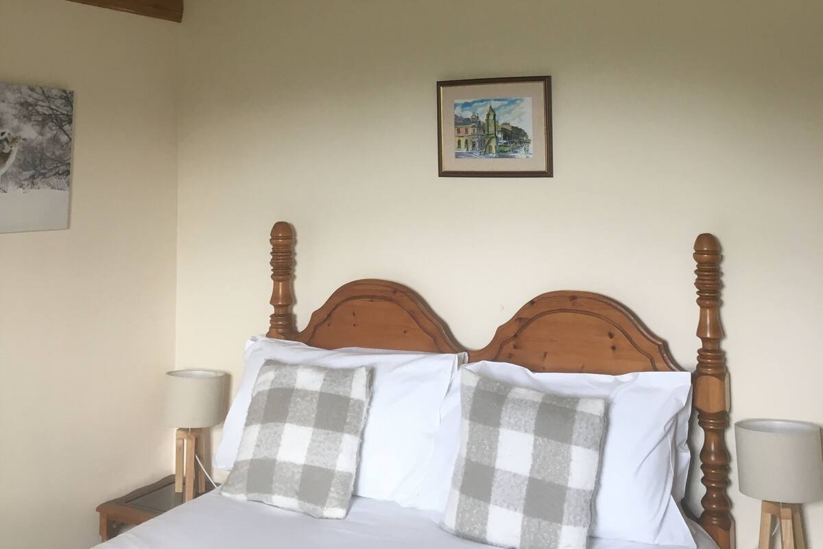 A bedroom with a wooden bed frame, white bedding, and a painting on the wall.