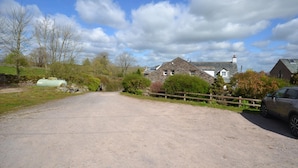 A rural road leading to a stone house with a white chimney, surrounded by trees and a wooden fence. - The Herdwick Inn (Penrith)