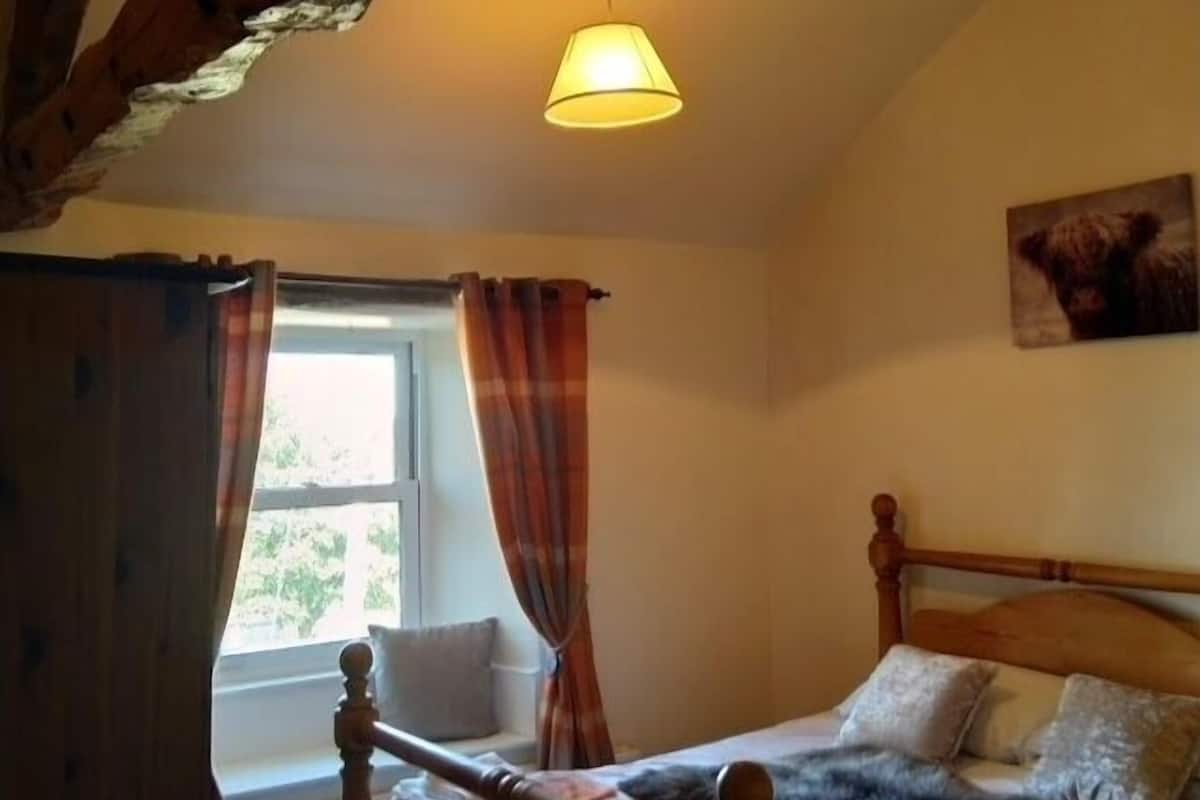 A bedroom with a wooden bed, a window with curtains, and a lamp.
