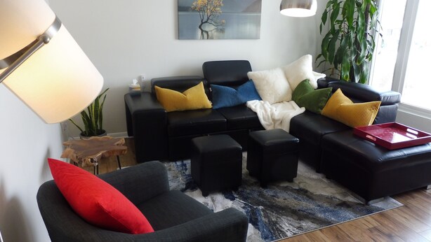 A modern living room with a black sofa set, a red chair, and a large plant.