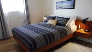 A neatly made bed with a striped bedspread, a bedside lamp, and a nightstand with a lamp.