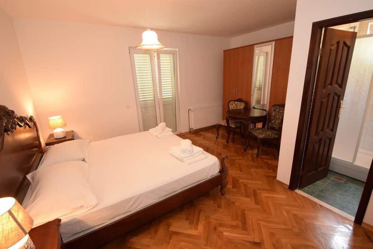 Ein Hotelzimmer mit Bett, Nachttisch, Lampe, Stuhl, Tisch und Tür.
