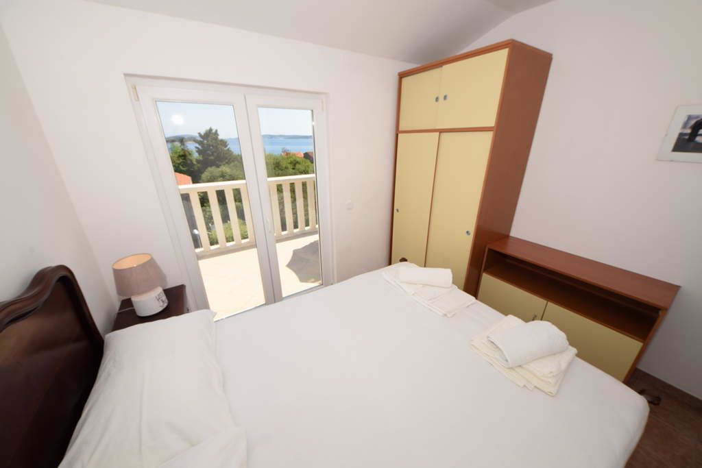 Ein Schlafzimmer mit Bett, Schrank, Nachttisch, Lampe und einem Balkon mit Meerblick.