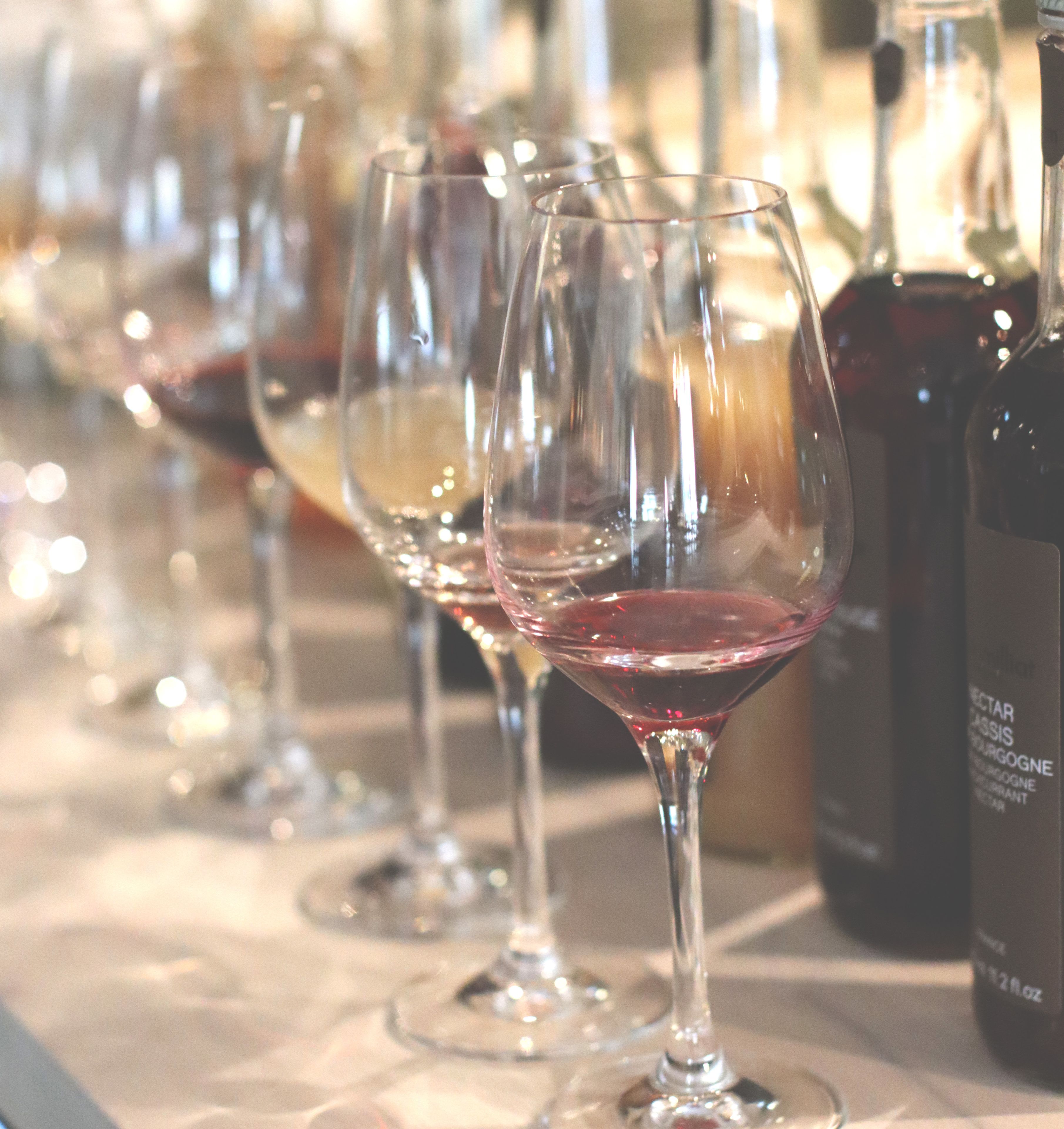 Una hilera de copas de vino sobre una mesa con botellas detrás.