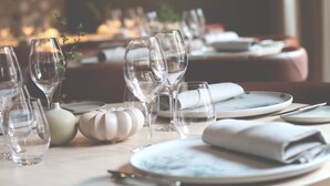 Mesa lista para comer, con cristalería transparente, platos y servilletas dobladas.