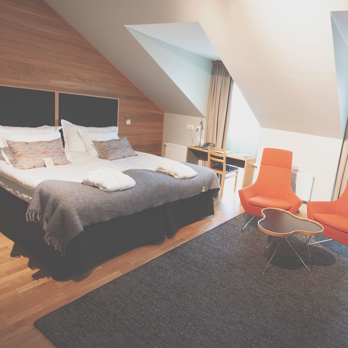 Ein modernes Schlafzimmer mit einem großen Bett, einem Schreibtisch und zwei orangefarbenen Stühlen.