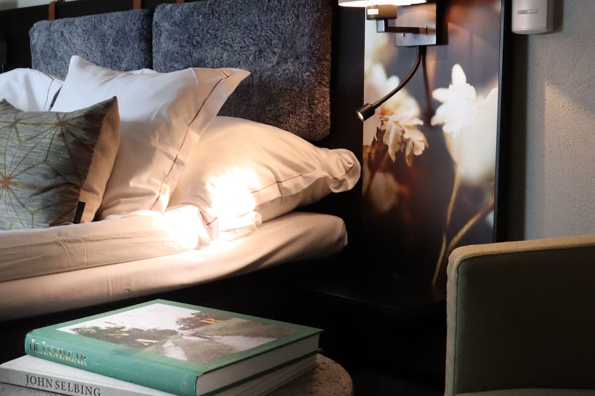 Un lit bien fait, avec des oreillers, une lampe de chevet et un livre posé sur la table de chevet.