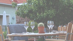 Un espacio exterior para comer con una mesa lista para dos personas, un cactus en maceta y un edificio con un letrero que dice 