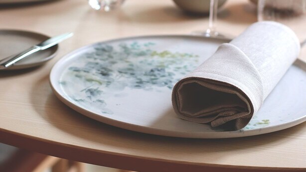 Una mesa puesta con un plato, una servilleta doblada y una cuchara.