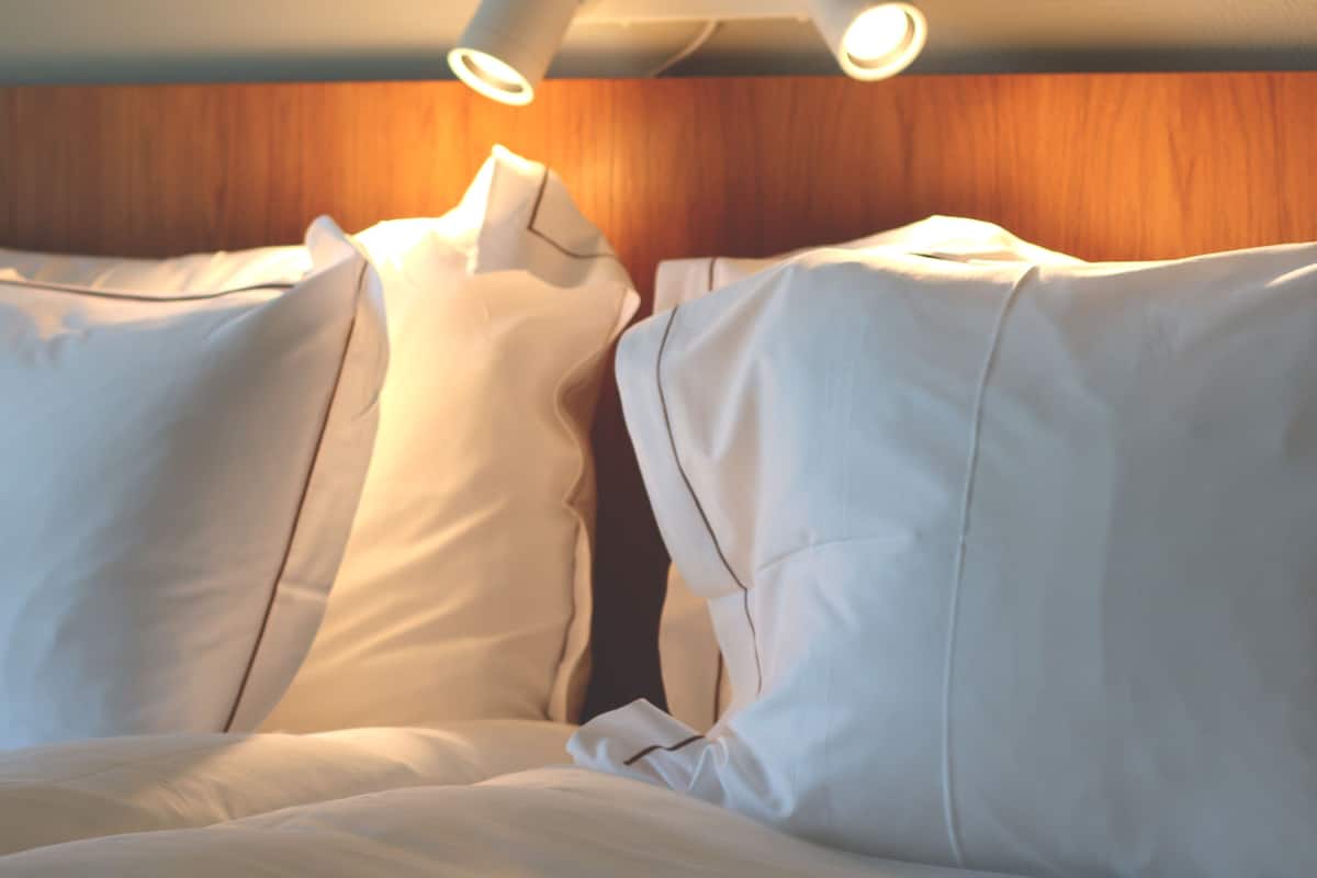 Un lit avec du linge de lit blanc et une tête de lit en bois.