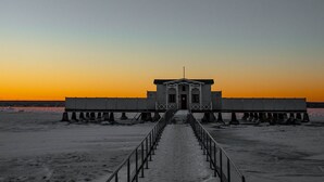 Un muelle que conduce a un edificio con puerta y ventanas, rodeado de agua y un cielo al atardecer.