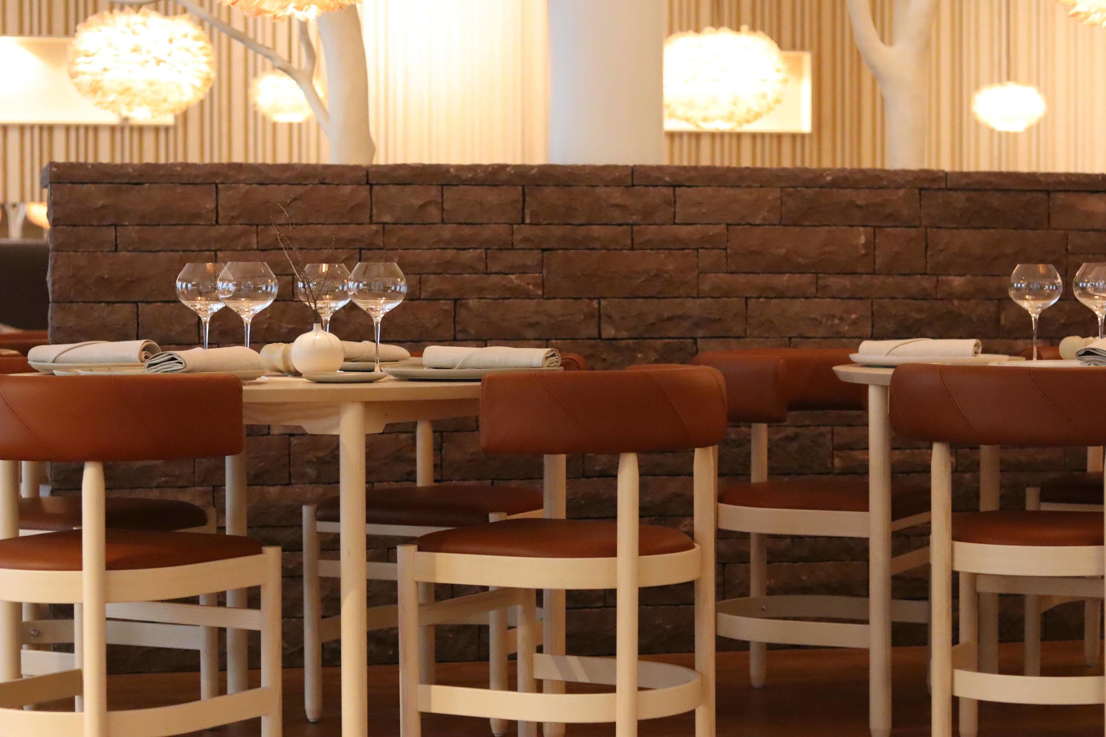 En restaurang med inredning som kännetecknas av tegelväggar, vita bord och bruna läderstolar.