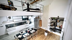 A modern kitchen with a dining area, featuring a black countertop, white cabinets, and a wooden dining table set for four. - Lussuoso Loft dei Giustiniani Acquario (Genoa)