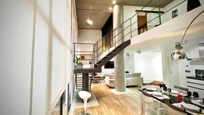 A spacious, modern interior with a wooden floor, a dining area with a long table and chairs, a staircase leading to an upper level, and a large pillar. - Lussuoso Loft dei Giustiniani Acquario (Genoa)