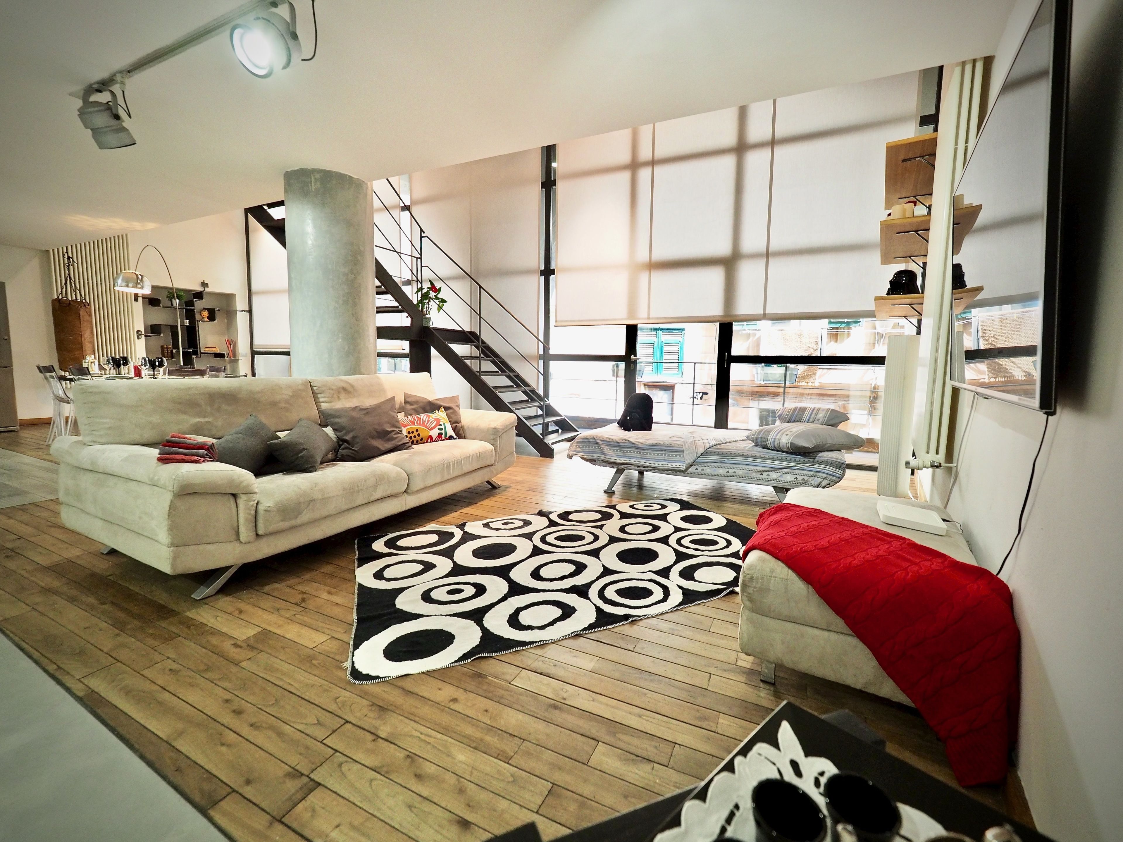 A modern living room with a sofa, coffee table, and patterned rug. A staircase is visible in the background, leading to an upper level.