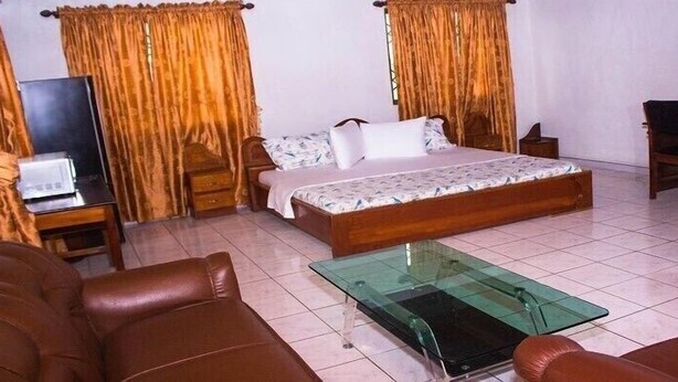 A bedroom with a bed, a glass coffee table, a sofa, and curtains. - Vinny Hotel (Sekondi-Takoradi)
