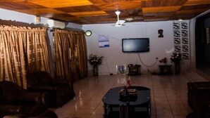 A living room with a flat-screen TV mounted on the wall, a ceiling fan, and a tiled floor. - Vinny Hotel (Sekondi-Takoradi)