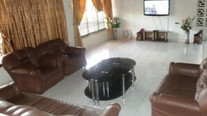 A living room with brown leather sofas, a black coffee table, and a television on the wall. - Vinny Hotel (Sekondi-Takoradi)