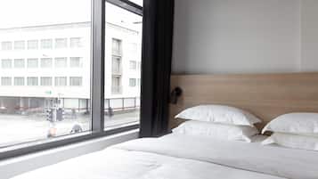 Een hotelkamer met een groot raam, een bed met witte lakens en een houten hoofdbord.