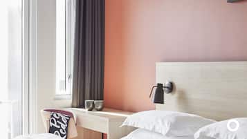 A hotel room with a bed, a bedside table, a lamp, and a window with curtains.