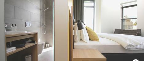 Una habitación de hotel moderna con ducha, una mesita de noche, una cama con almohadas, una ventana y vistas a la ciudad.