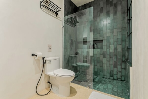 A modern bathroom with a toilet, a glass-enclosed shower, and a tiled floor. - Mamachá Natural Residence (Valladolid)