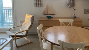 A dining area with a round wooden table, white chairs, a sailboat model, and a pendant light.