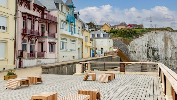 A wooden deck with benches, a stone wall, and colorful buildings with balconies.