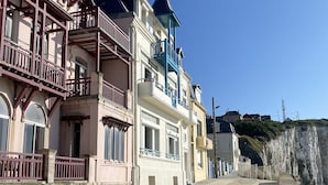 A coastal street with multi-story buildings, balconies, and a clear sky.