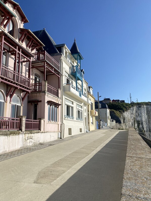 A coastal street with multi-story buildings, balconies, and a clear sky.