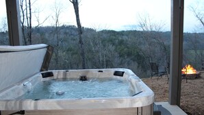 A hot tub with a wooden exterior, surrounded by a deck area with outdoor seating and a fire pit.