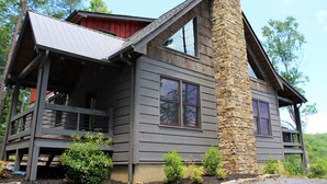 A two-story house with a stone chimney, a balcony, and a view of the surrounding forest.