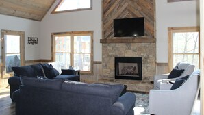 A living room with a stone fireplace, two sofas, and a television mounted on the wall.