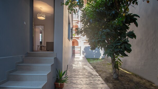 A narrow, sunlit corridor with a staircase leading to a door, surrounded by walls and a potted plant. - Ithaka Deluxe Home (Zakynthos)