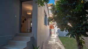 A modern building with a staircase leading to an entrance, a small garden area with a potted plant, and a view of a neighboring building. - Ithaka Deluxe Home (Zakynthos)