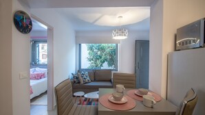 A modern living room with a sofa, dining table, and chairs. There is a window with a view of greenery outside. - Ithaka Deluxe Home (Zakynthos)
