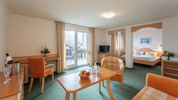 A hotel room with a dining table, two chairs, a sofa, a TV, a bed, and a window with curtains.