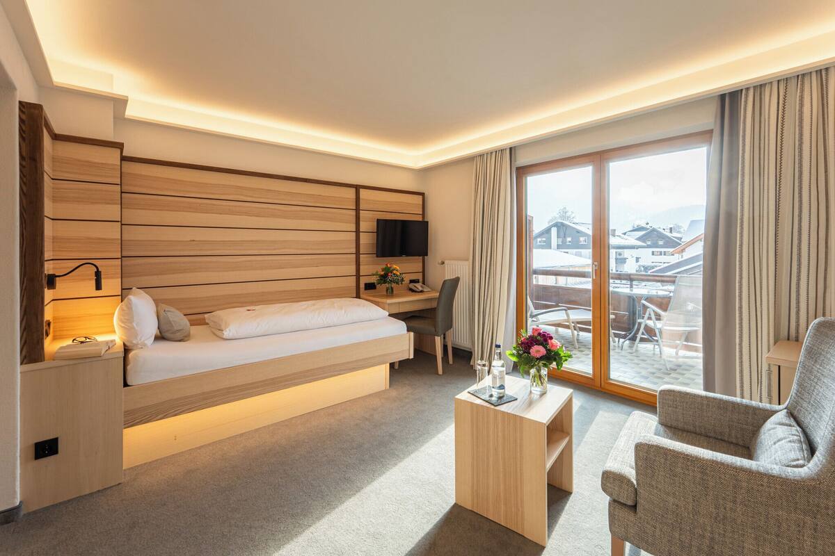 Une chambre d’hôtel moderne équipée d’un lit, d’un bureau et d’une chaise, d’une télévision et d’une grande fenêtre donnant sur des immeubles.