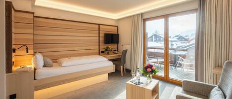 A modern hotel room with a bed, desk, and chair, a TV, and a large window with a view of buildings.