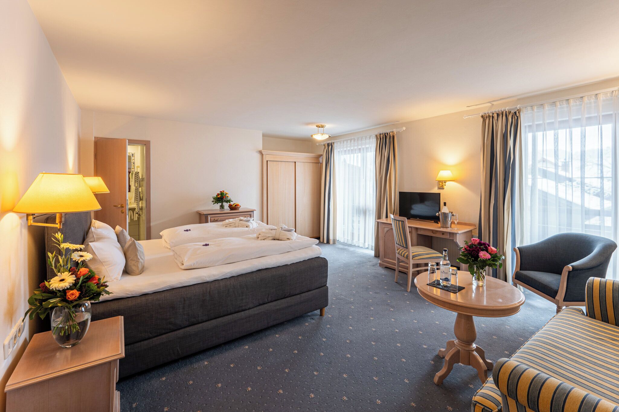 Una camera d'albergo con un letto, una scrivania, una televisione, una sedia e un tavolo con fiori.