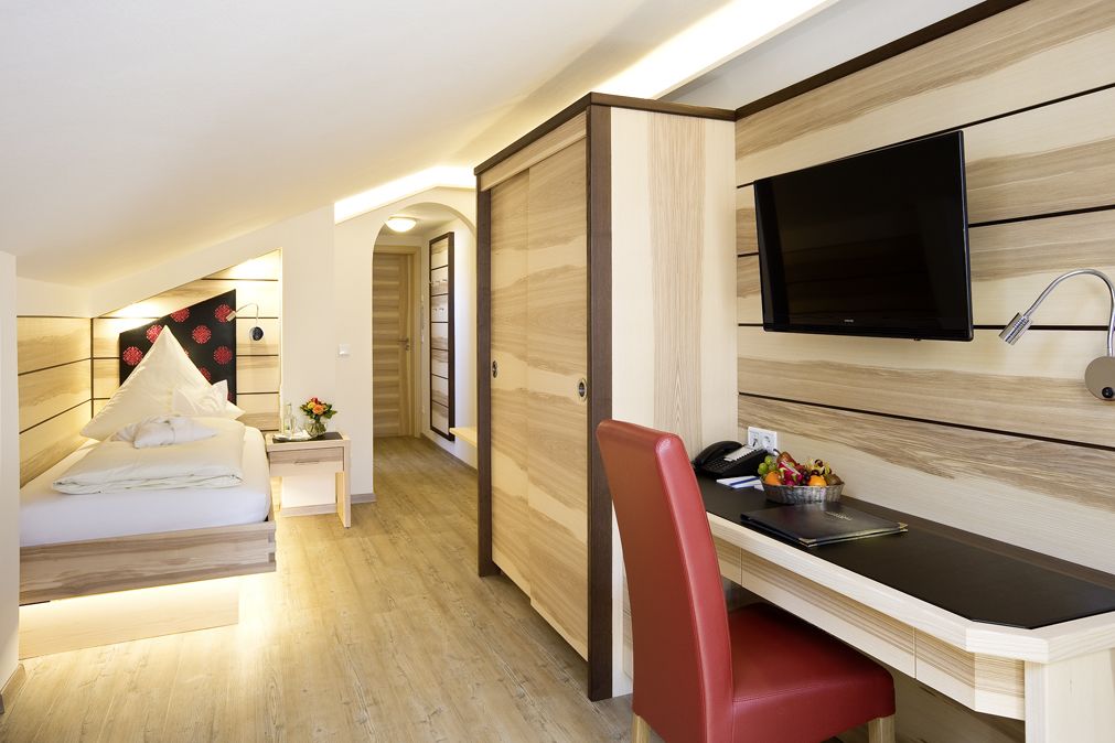 A modern hotel room with a bed, a desk with a chair, a TV, and a bathroom.