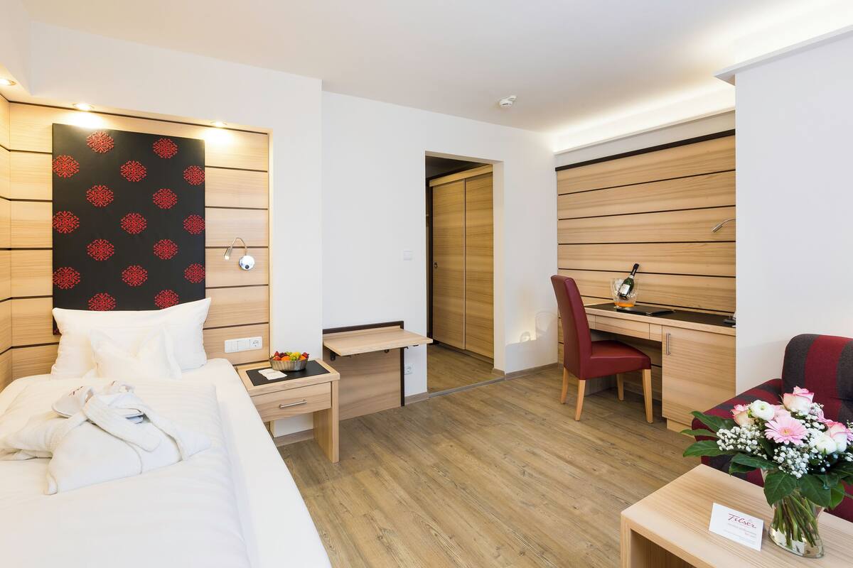 Une chambre d’hôtel moderne, équipée d’un lit, d’un bureau, d’une chaise et d’une petite table sur laquelle est posé un vase de fleurs.