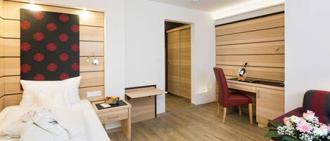 A modern hotel room with a bed, a desk, a chair, and a small table with a vase of flowers.