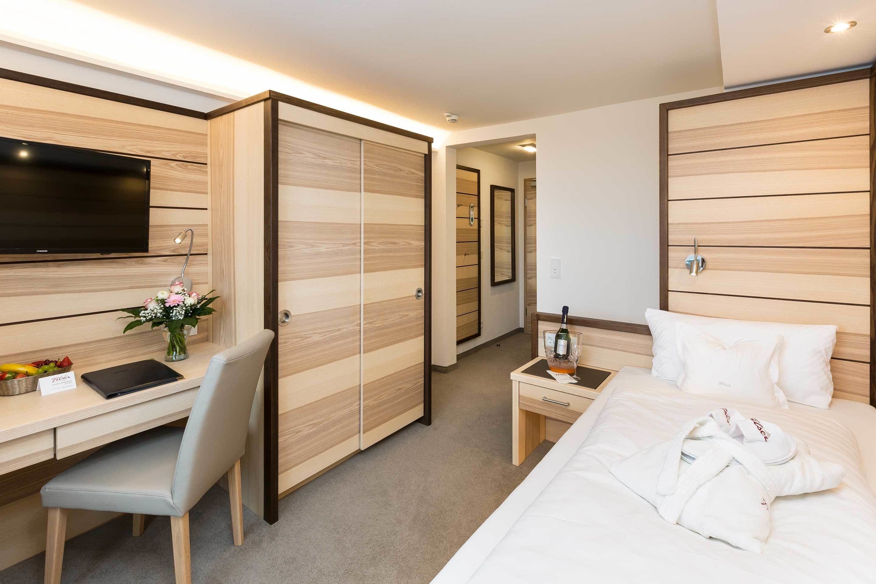 Habitación de hotel con cama, escritorio, silla, televisión, mini bar y armario.