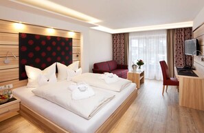 A hotel room with a large bed, a desk, a chair, a TV, and a window with curtains. - Hotel Filser (Oberstdorf)