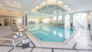 An indoor swimming pool with lounge chairs, a tiled floor, and a ceiling with a geometric pattern. - Hotel Filser (Oberstdorf)