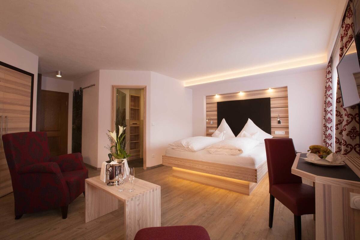 Une chambre d’hôtel moderne, équipée d’un lit, d’un bureau, de deux chaises et d’une petite table sur laquelle est posé un vase de fleurs.